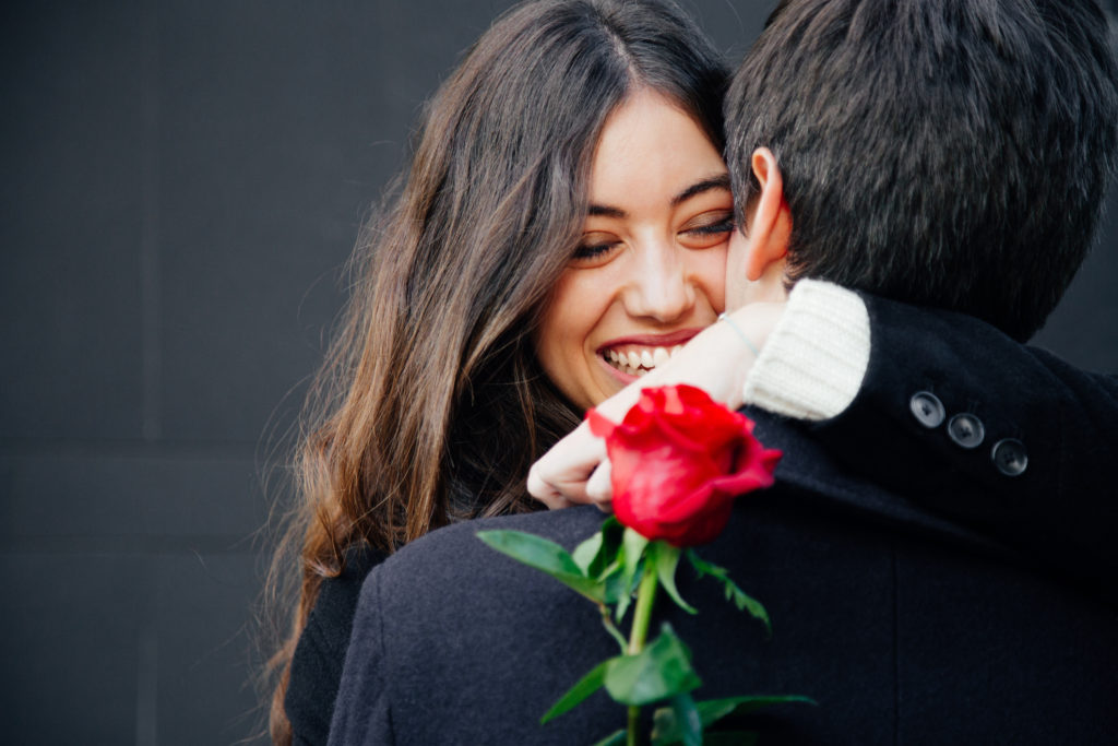 Beautiful and happy young woman in love hugging her husband holding a red rose