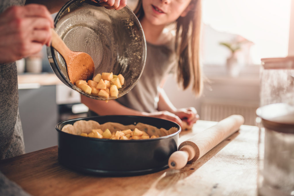 Woman pouring apple filling into baking pan her daughter standing beside her and helping
