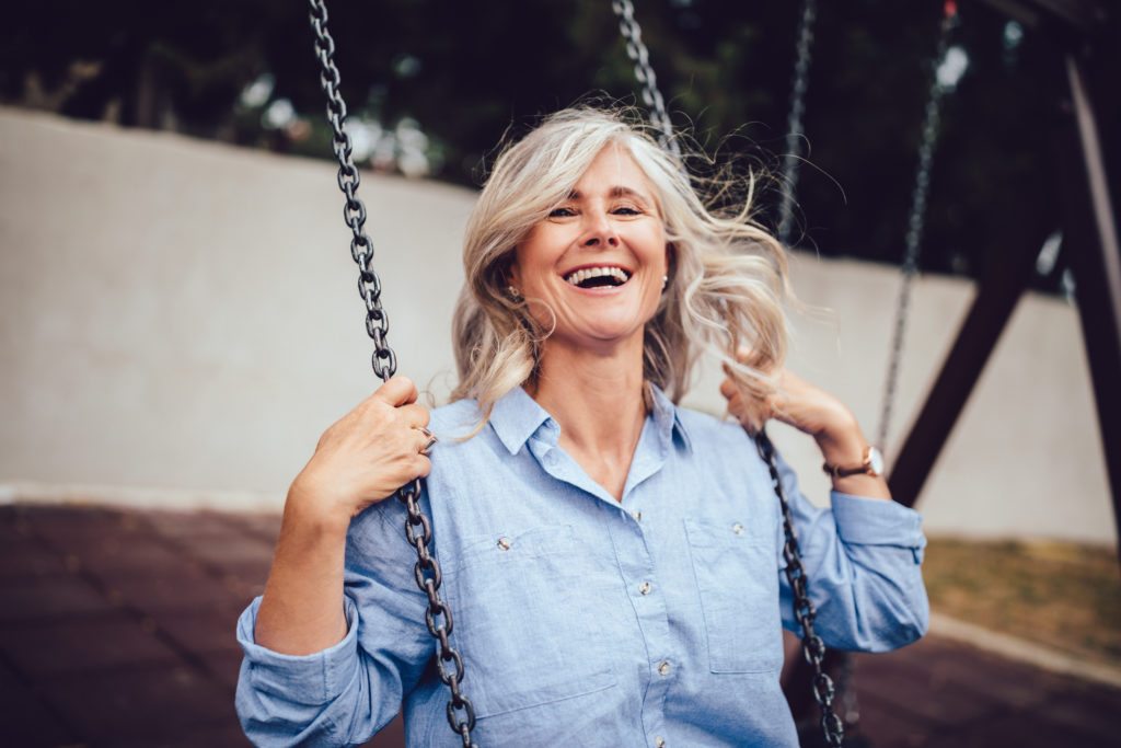 joyful senior woman with gray hair sitting on swing, having fun and enjoying retirement