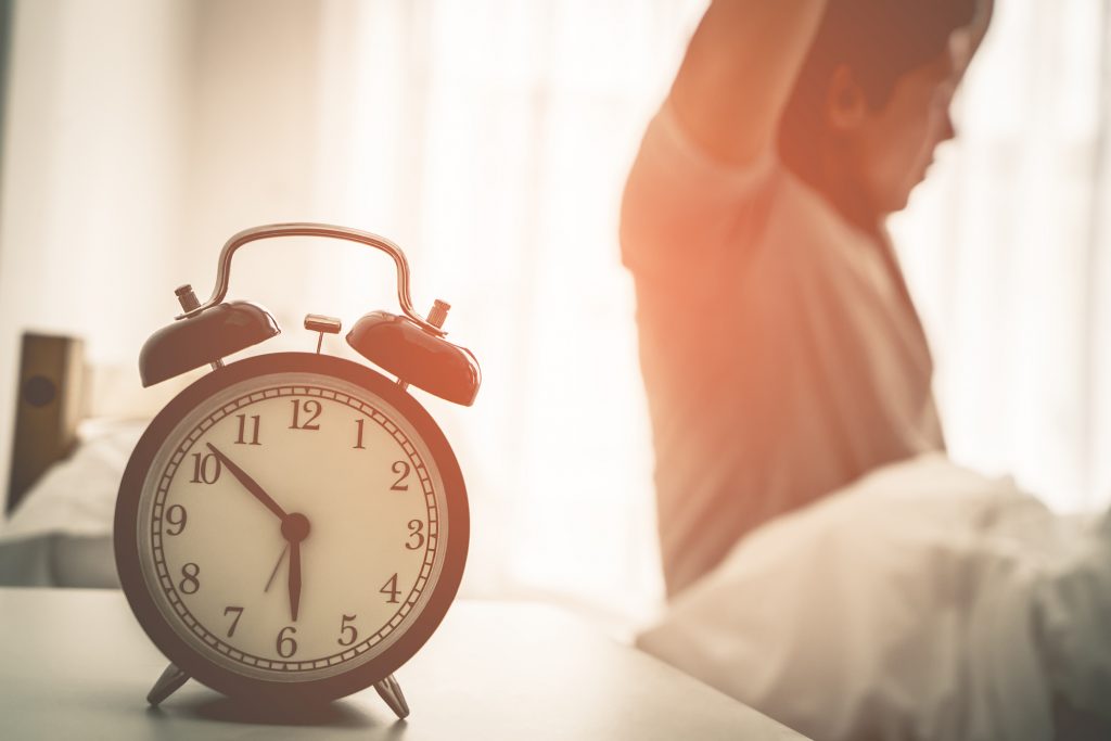 Man stretching behind alarm clock