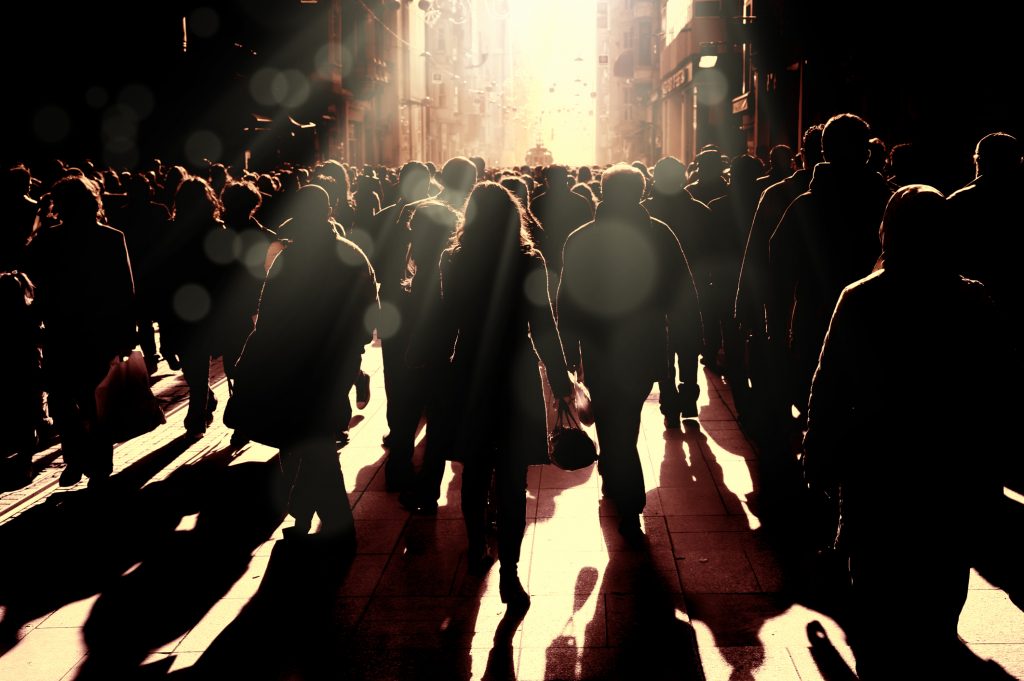 Large group of silhouetted people walking on busy street