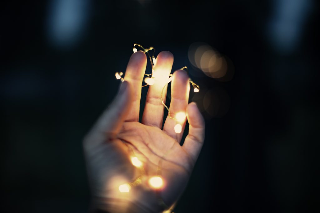 a woman holding string lights in her hand in a dark place