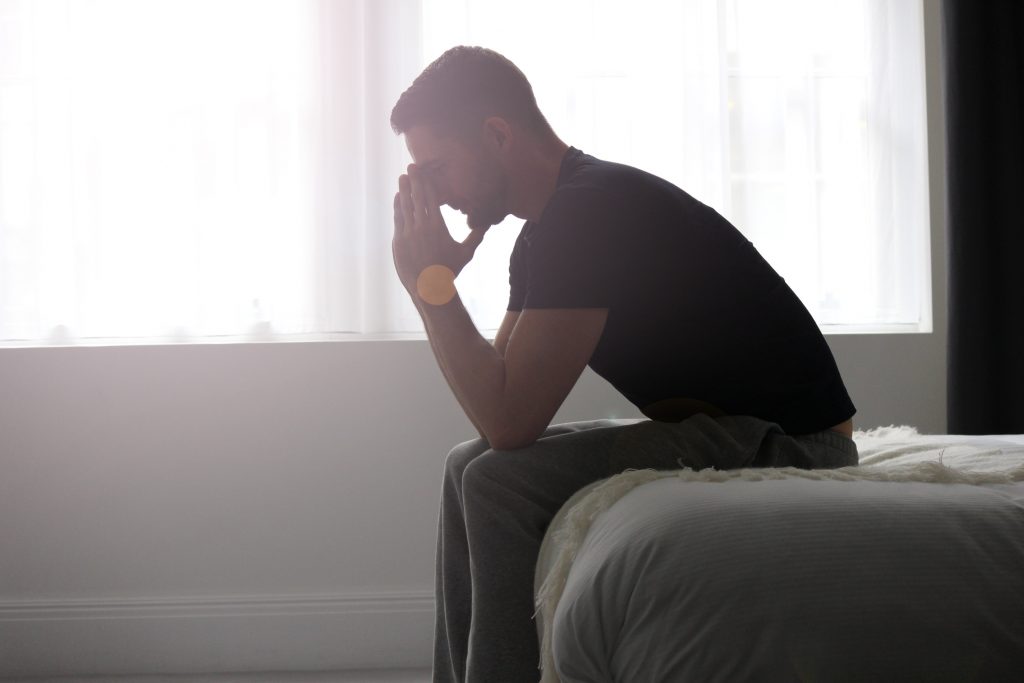 overwhelmed man sitting on edge of bed with face in hands