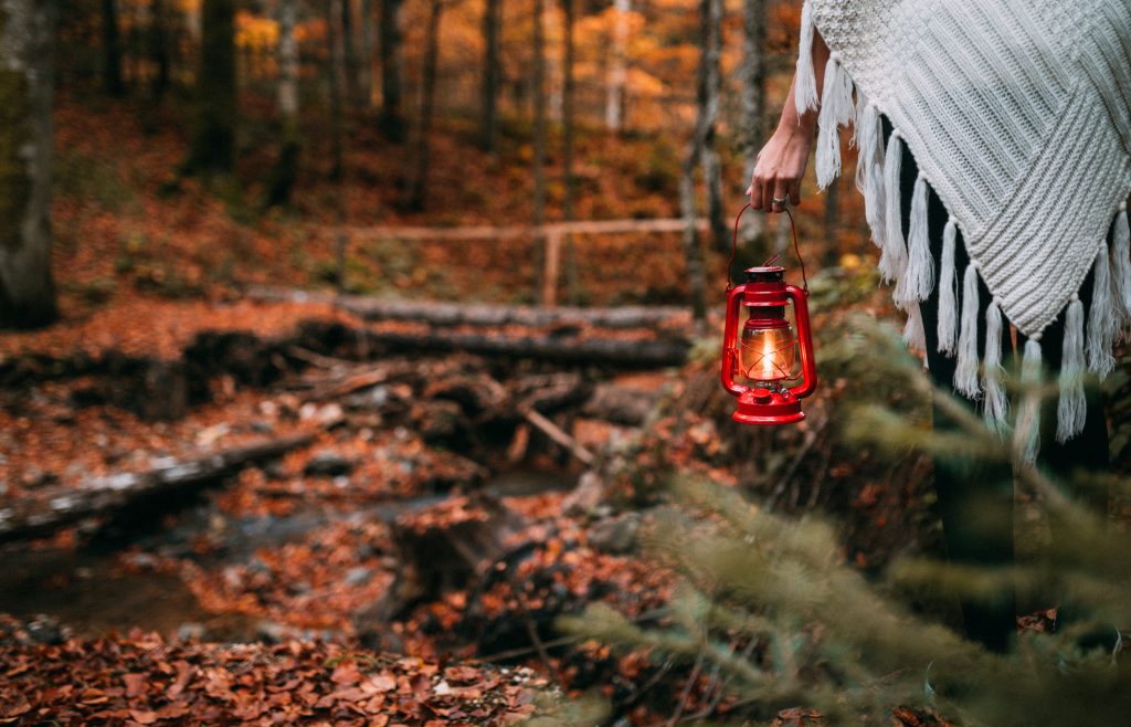 Rearview of a woman in a white poncho holding an old red lantern while walking through the forest.