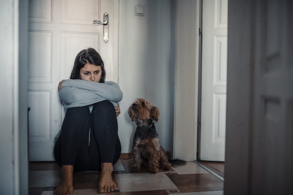 Woman feeling lonely is sitting desperate on the floor and crying and her dog is next to her