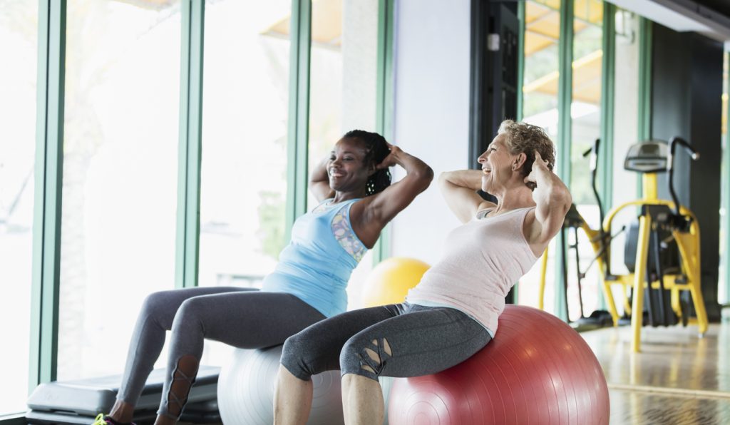 Two women at the gym on medicine balls, talking and making a change
