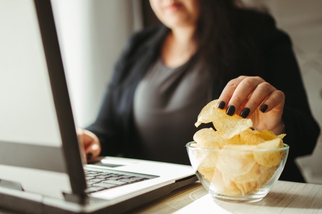 Woman mindlessly eating chips from bowl at her workplace