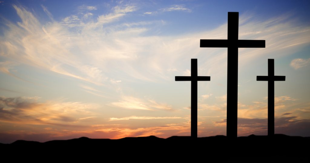 Easter. The crucifixion. Three wooden crosses in silhouette stand silently on a hill at sunset. The dramatic sky is beautiful in its blue and orange colors. Christianity, religious themes.