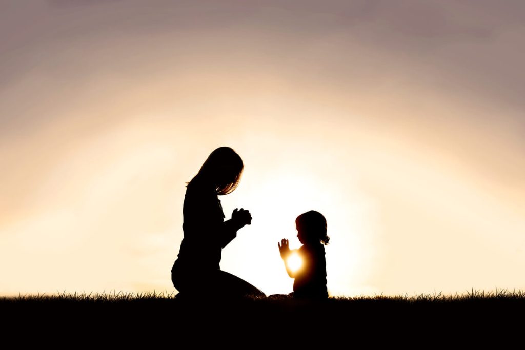 A mother and her daughter praying in the sunset