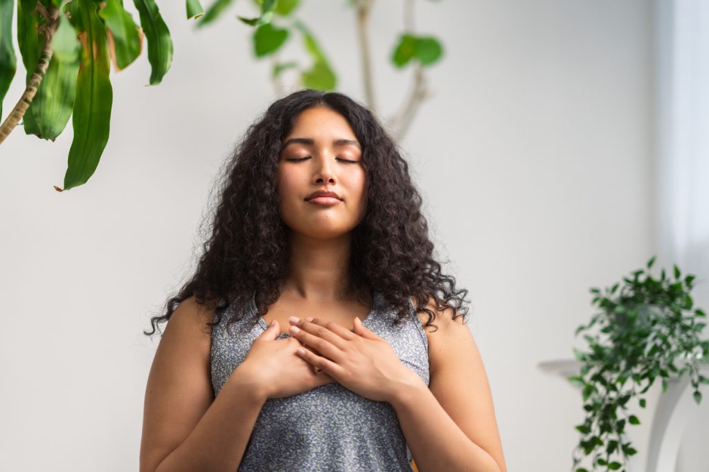 A beautiful and young multiracial woman is doing breathing exercise to help with panic attack.