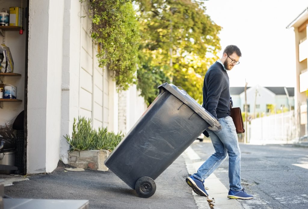 Man pulling a wheeled dumpster out of his garage while going to work so the nagging will stop