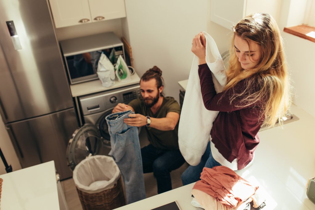 Happy couple folding their clothes and arranging them after wash. Couple doing their laundry work together at home and coping with changes in their relationship.