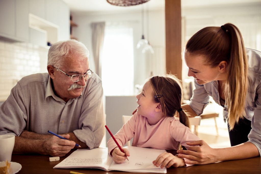 Close up of a grandfather helping out his granddaughter with schoolwork. Mom, who is sandwich generation, is watching