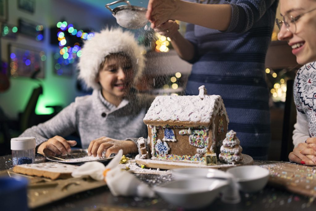 Christmas traditions: Mother is dusting sugar on gingerbread house