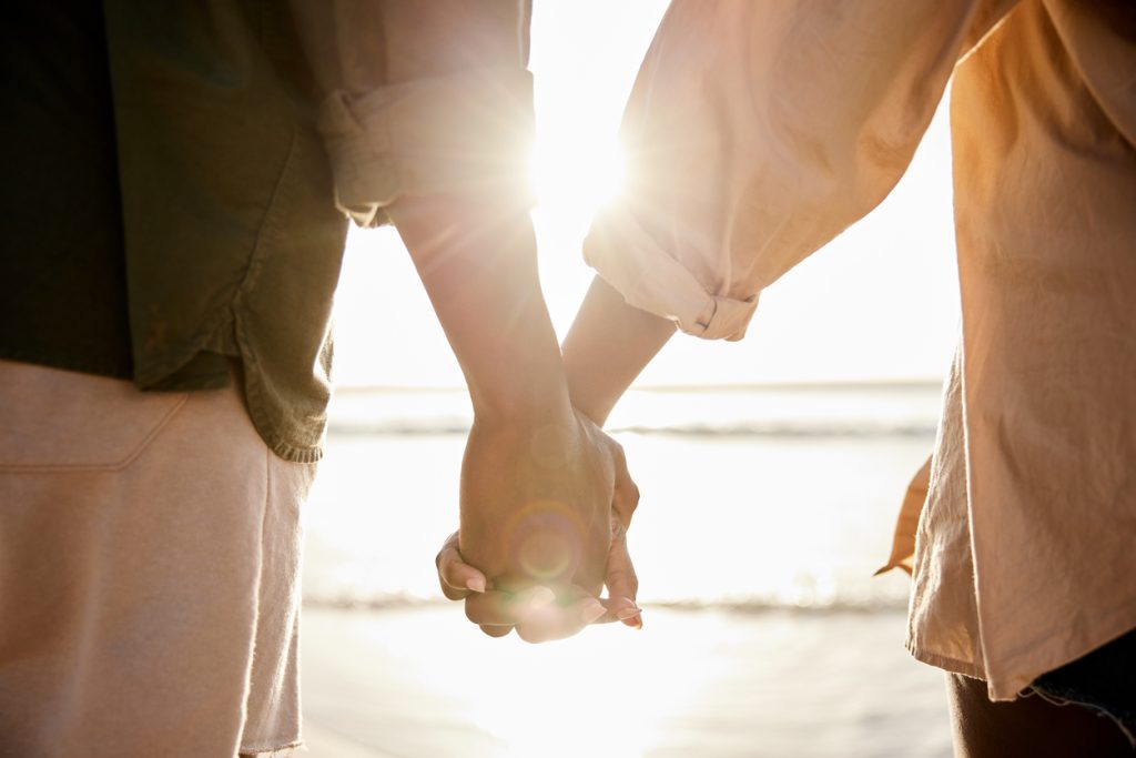 Couple holding hands together on a beach at sunset stock photo