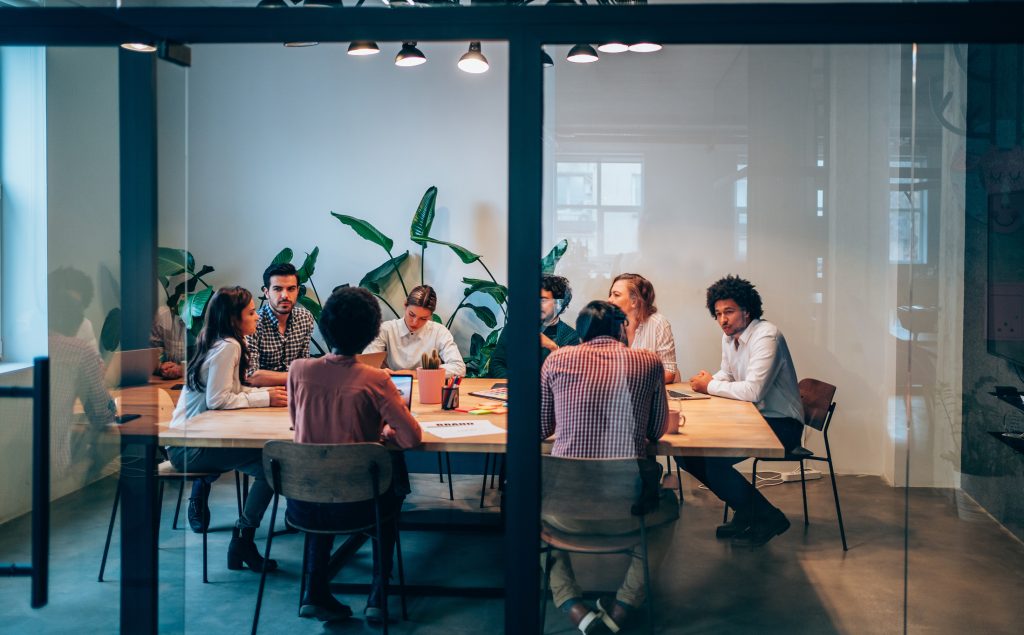 Group of young business people working together in creative office. Multi-ethnic group of business persons on a meeting in modern office. Shot of a group of people sitting on a conference table in board room. The view is through glass. Emotional Intelligence
